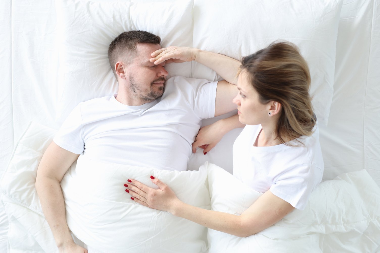 Married Couple Is Lying in Bed Top View. Man Holding His Head